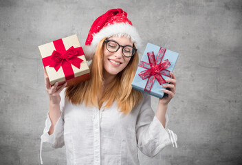 Santa woman holding christmas gifts isolated on gray background. Happy young girl wearing red santa hat and holding present box