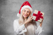 © Alen-D - Lovely woman wears christmas santa claus hat - cap and holding red gift box - present with ribbon, isolated on gray background
