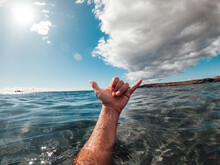 Man Hands In Surf Sign Hallo Out Of The Blue Ocean Water With Coast And Nice Sky In Background - Concept Of People And Summer Holiday Vacation