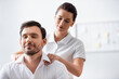 © LIGHTFIELD STUDIOS - Masseuse massaging shoulders of smiling businessman with closed eyes on blurred background