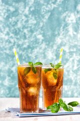 The glass of iced tea with blackberry on wooden table. Cuba Libre or long island cocktail, cold drink or lemonade with lemon and basil. Green turquoise on background