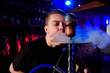 Man smoking traditional hookah pipe and exhaling smoke in hookah cafe.