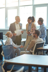 Wall Mural - Vertical shot of cheerful multiracial business people having a meeting in the modern office, discussing work and smiling