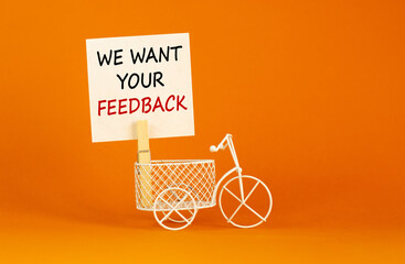 Wall Mural - Wooden clothespin with white sheet of paper. Text 'we want your feedback'. Miniature bicycle model. Beautiful orange background. Business concept, copy space.