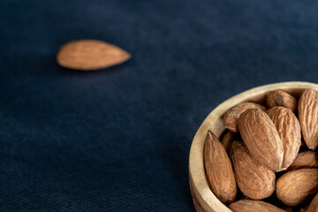 Almonds in a wooden bowl on a black table. Close-up and minimalist shot. top view