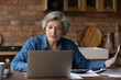 © fizkes - Smiling mature woman using laptop, online baking service, checking financial documents at home, senior grey haired female sitting at table with domestic bills and calculator, accounting