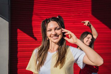 Two beautiful friends smiling and enjoying the day - Beautiful girl posing for the photo while her friend in the back jokes pointing at her - Two pretty friends smiling on a sunny afternoon.