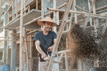 builder holds shovel while bringing sand to sift on strimin wire against house building background