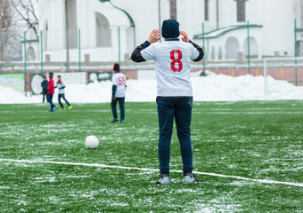 Wall Mural - Boys in white sportswear running on soccer field with snow on background. Young footballers dribble and kick football ball in game. Training, active lifestyle, sport, children winter activity