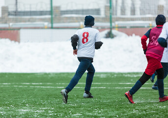 Wall Mural - Boys in white sportswear running on soccer field with snow on background. Young footballers dribble and kick football ball in game. Training, active lifestyle, sport, children winter activity