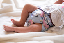 A Baby Lying On A Bed With A White Blanket Where The Focus Is On Her Legs And Non Disposable Diaper.