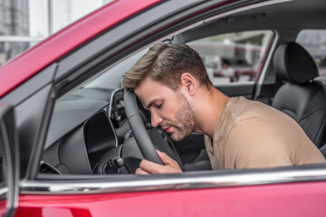 Wall Mural - Tired young male resting his head on steering wheel