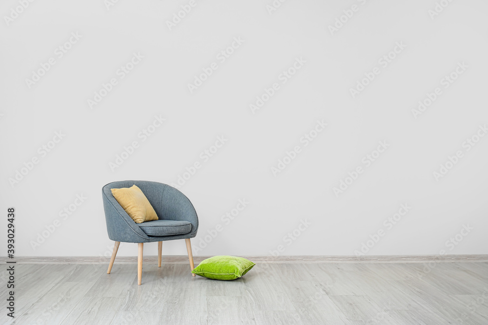 Stylish armchair with pillows near light wall in room