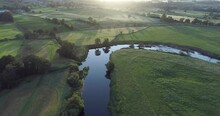 Aerial Shot Of Fields And A River In The English Countryside At Sunrise.