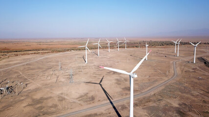 Windmills in the steppe. Near a small town. Alternative, clean energy. Top view from the drone on the long blades. The propeller spins, shadows fall to the ground. Orange sand, near a farm. Kazakhstan