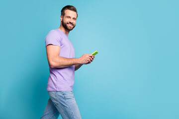 Wall Mural - Photo portrait of happy millennial browsing internet with cellphone smiling isolated on vivid blue color background with copyspace