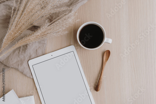Obraz Dibond Flatlay of blank screen tablet, coffee cup, pampas grass on beige wooden background. Home office desk workspace. Lady, girl boss business, work template with mockup copy space. Flat lay, top view.