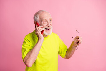 Wall Mural - Photo of old cheerful positive man hold glasses wear lime t-shirt talk speak phone isolated on pink color background