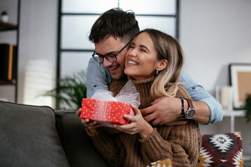 Wall Mural - Boyfriend surprising his girlfriend with a gift. Young man giving a gift box to his girlfriend.