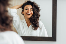 Happy Woman In Bathroom. Young Female Playing With Her Hair In Front Of A Mirror.