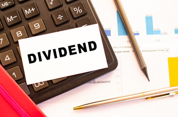 Text DIVIDEND on white card with metal pen, calculator and financial charts. Financial concept.