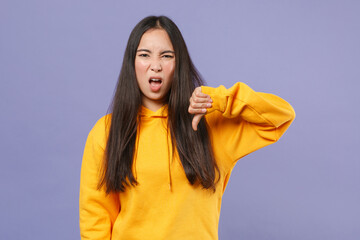 Wall Mural - Disgusted displeased dissatisfied young brunette asian woman wearing casual basic yellow hoodie standing showing thumb down looking camera isolated on pastel violet colour background studio portrait.