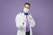 © ViDi Studio - Young doctor man in medical gown stethoscope face mask safe from coronavirus virus covid-19 point index fingers on camera isolated on violet background. Healthcare personnel health medicine concept.