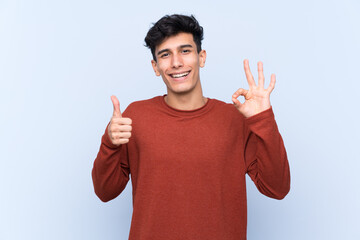 Young Argentinian man over isolated blue background showing ok sign and thumb up gesture