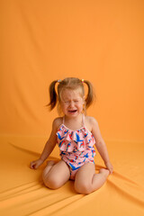 a little girl at the age of one and a half years sits on her lap and cries on a yellow background. t