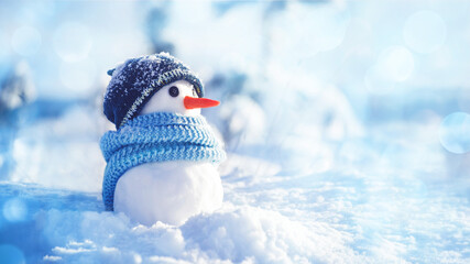 Little snowman in a hat and scarf on the snow on a sunny winter day, soft selective focus, copy space. Christmas background banner, winter holidays, preparation for the holiday