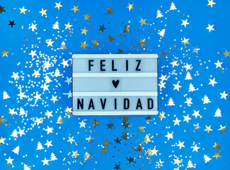 Light box with Feliz Navidad phrase, Spanish Merry Christmas on a blue background with confetti.