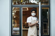 © Prostock-studio - Coffee shop owner, barista young african american man in protective mask opens front door at start of working day