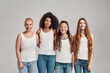 © Svitlana - Portrait of four young diverse women wearing white shirts and denim jeans smiling at camera while posing together isolated over grey background