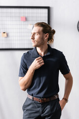 Wall Mural - Confident businessman with hand in pocket looking away while standing in office with blurred mesh organizer on background