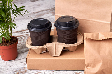 Two closed paper cups of coffee in cupholder. Kraft paper packaging on the wooden table.