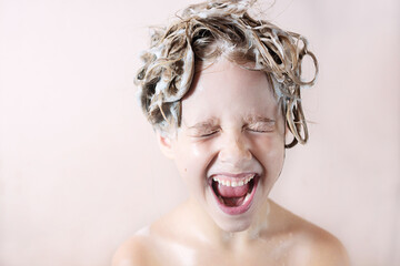 Wall Mural - a little blonde girl in the bathroom with foam on her head laughs happily with her mouth open