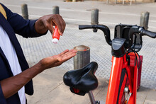 Detail of a black man hands using disinfectant gel in front of a public bike parked on the street