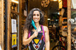 © David Fuentes/ADDICTIVE STOCK - Positive adult ethnic female mechanic in colorful apron with protective mask smiling and looking at camera while standing on entrance of bike service workshop