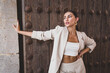 © Jose Carlos Gutierrez/ADDICTIVE STOCK - Delightful slim ethnic female model with perfect makeup wearing stylish light suit standing against weathered wooden door of urban building