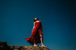 © Lucia Romero/ADDICTIVE STOCK - From below low angle of barefoot female in long red dress standing with eyes closed on rough hill