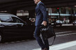 © Maskot - Midsection of businessman with bag and smart phone in city