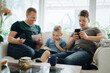 © Maskot - Smiling father with smart phone looking at son using digital tablet on sofa at home