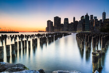 Scenic View Of Mooring Posts In East River With Brooklyn Bridge Park In Background During Sunset