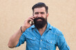 © Volodymyr - Portrait of stylish handsome young man with beard standing outdoors and leaning on wall. Smiling man using mobile phone.