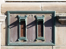 Old British Postal Mail Boxes With Rusted Letter Slots And Ornate Green Copper Frames With The Words Postage Stamps Surrounded By An Old Stained Metal Frame On S Stone Wall