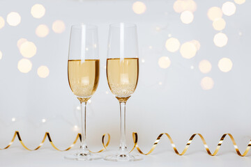 Wall Mural - Two glasses of champagne with lights and ribbons on a white background holiday