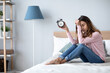 © BestForYou - Unhappy woman with closed eyes holding alarm clock on the bedю