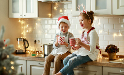 Poster - happy children on Christmas eve,   girl and boy drink hot cocoa drink that they baked together in cozy kitchen at home.