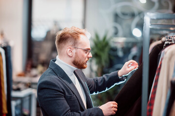 blonde millennial man in a business attire chooses clothes in a store. The man is shopping.