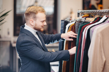 blonde millennial man in a business attire chooses clothes in a store. The man is shopping.